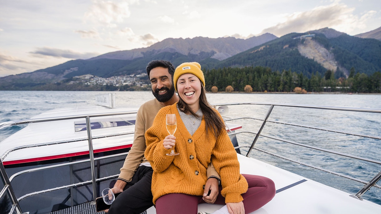 Couple enjoying wine on a boat with Queenstown mountains in the background on Lake Wakatipu.