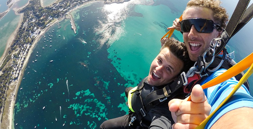 Tandem skydivers smiling during freefall over Rottnest Island, Australia.