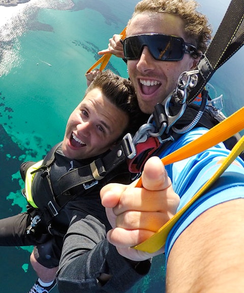Tandem skydivers smiling during freefall over Rottnest Island, Australia.