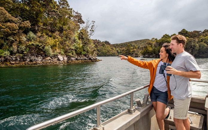 Couple on boat enjoying scenic view of lush forested shoreline.