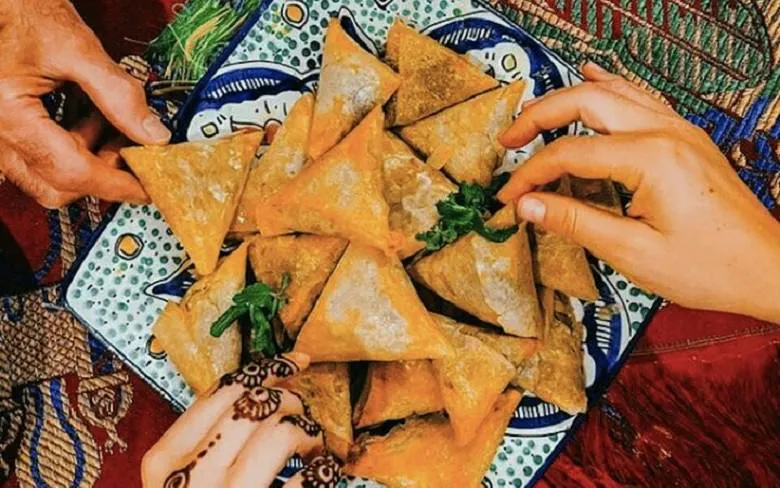 Hands reaching for Moroccan pastries on a decorative plate during cooking class in Marrakech.