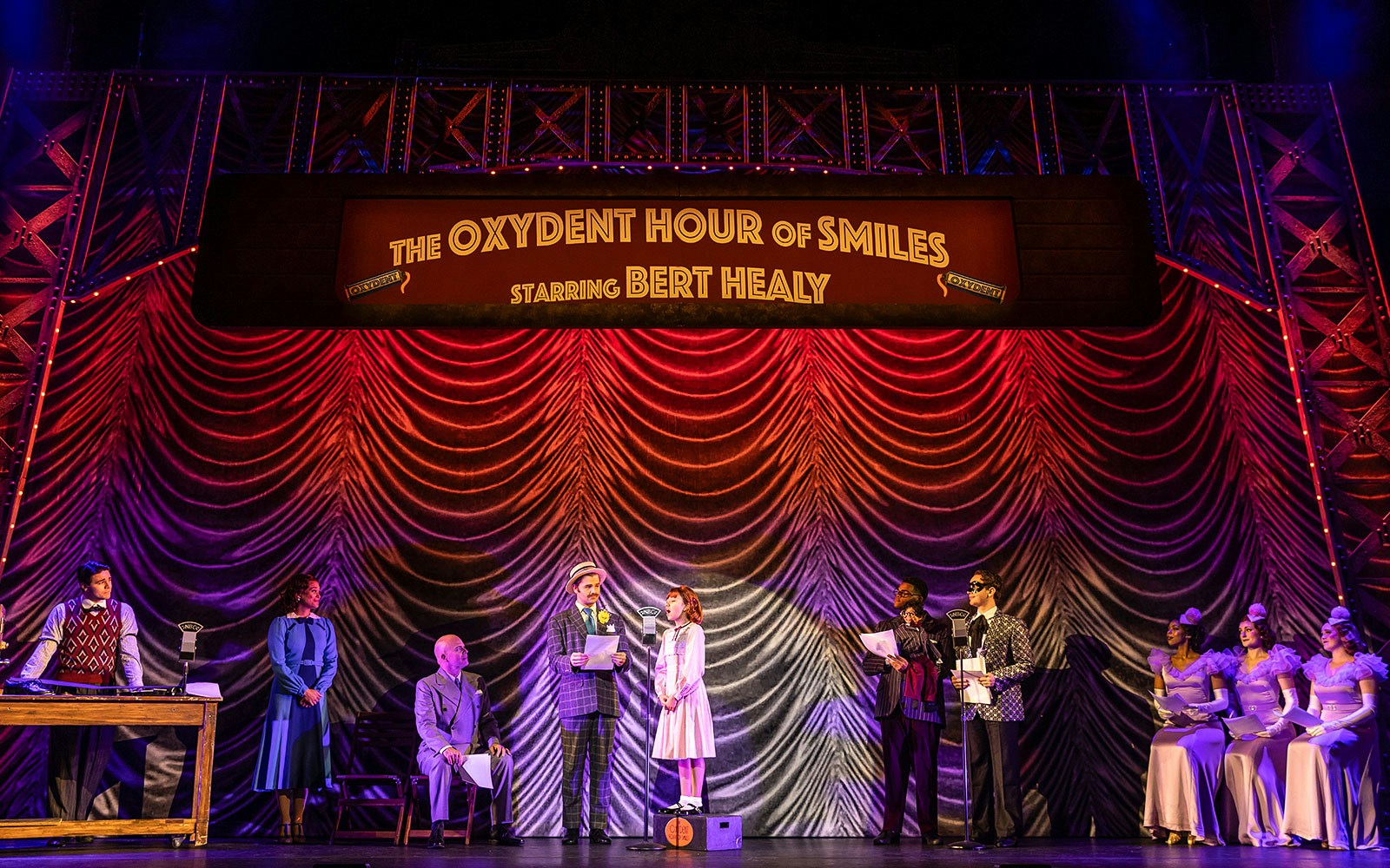 Stage performance of "Annie" with actors in period costumes under "The Oxydent Hour of Smiles" sign.