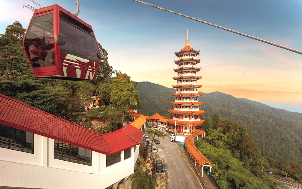 Genting Awana SkyWay cable car near pagoda tower in lush mountain landscape.