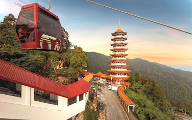Genting Awana SkyWay cable car near pagoda tower in lush mountain landscape.