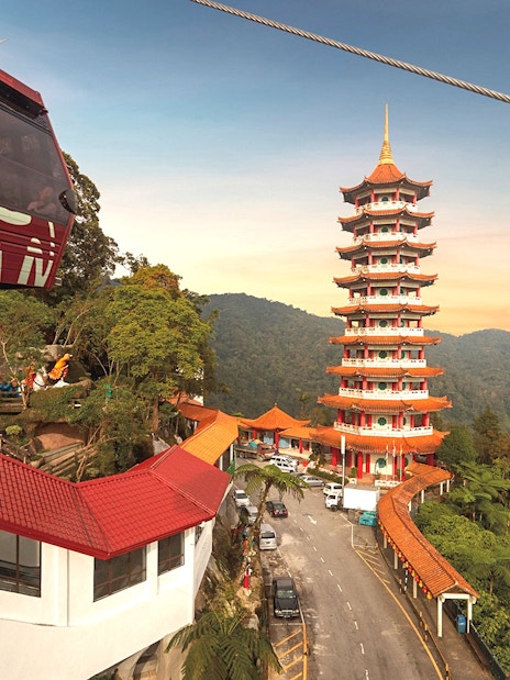Genting Awana SkyWay cable car near pagoda tower in lush mountain landscape.