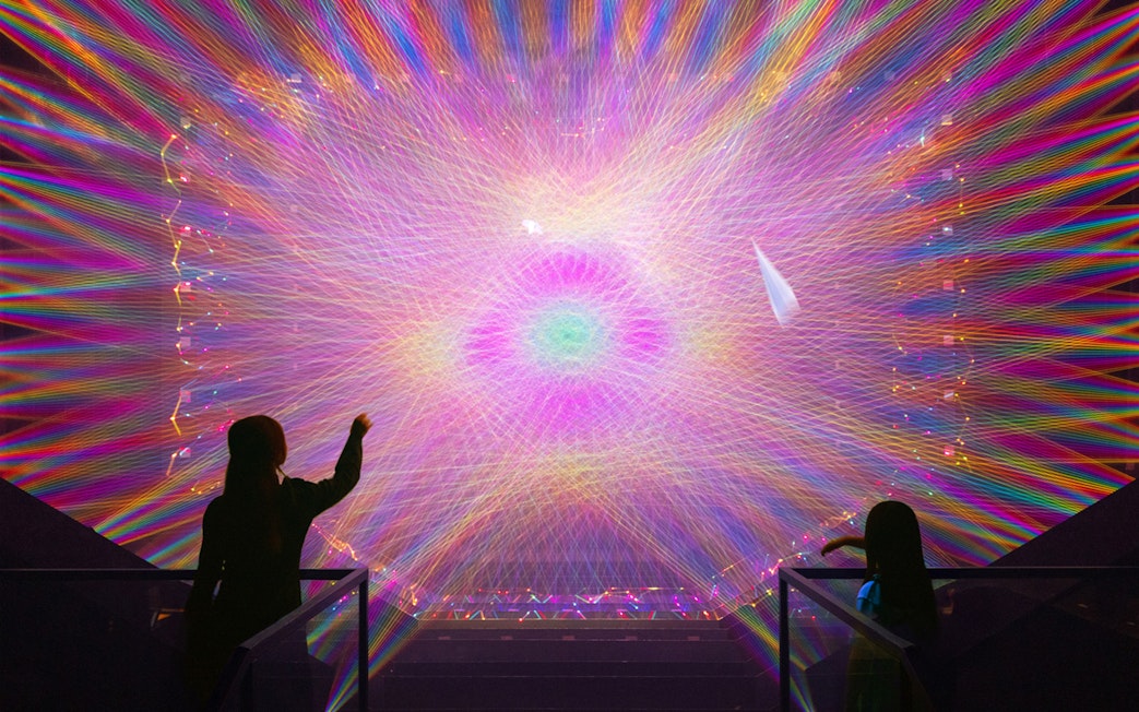 Two figures observe a vibrant digital light installation with colorful patterns.