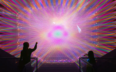 Two figures observe a vibrant digital light installation with colorful patterns.