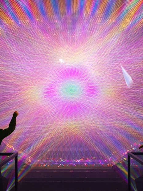 Two figures observe a vibrant digital light installation with colorful patterns.