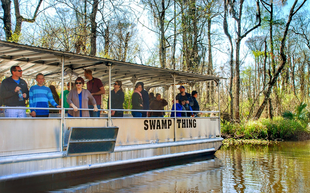 Tourists on a boat during a Swamp Tour near Oak Alley Plantation, surrounded by trees and water.