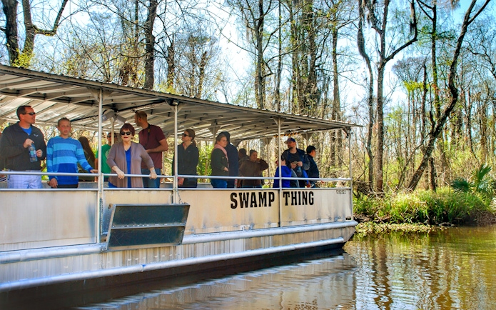 Tourists on a boat during a Swamp Tour near Oak Alley Plantation, surrounded by trees and water.