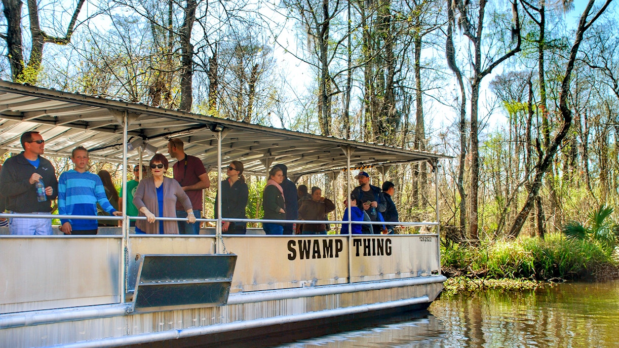 Tourists on a boat during a Swamp Tour near Oak Alley Plantation, surrounded by trees and water.