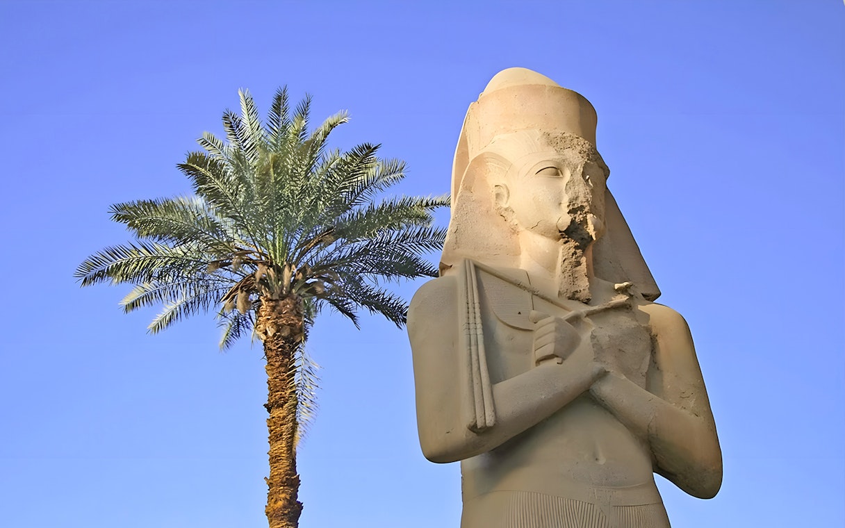 Statue of ancient Egyptian pharaoh at Karnak Temple with palm tree, Luxor, Egypt.