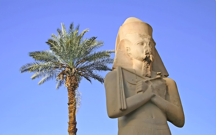 Statue of ancient Egyptian pharaoh at Karnak Temple with palm tree, Luxor, Egypt.