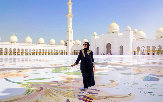Sheikh Zayed Grand Mosque courtyard in Abu Dhabi with a visitor walking.