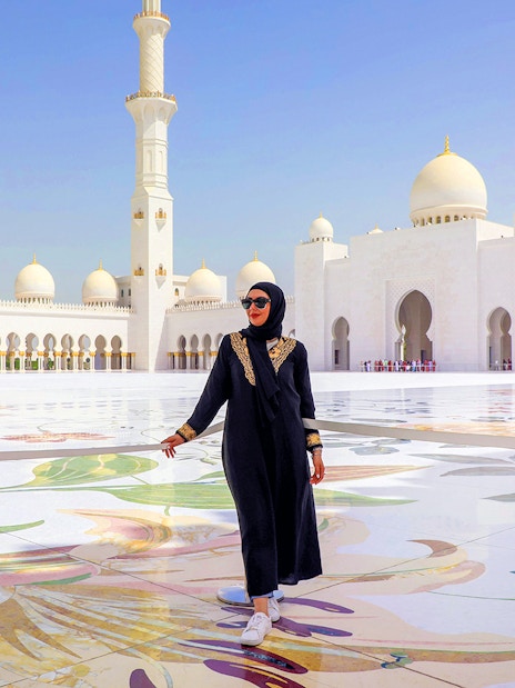 Sheikh Zayed Grand Mosque courtyard in Abu Dhabi with a visitor walking.
