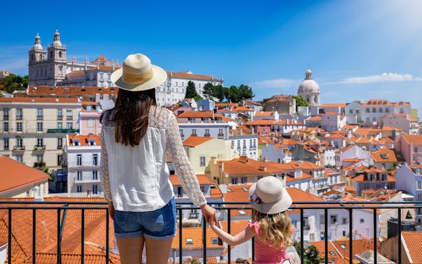 Woman and child overlooking Lisbon's rooftops with St. George’s Castle in the background.
