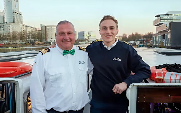 Boat crew on Amsterdam canal cruise with cityscape in background.