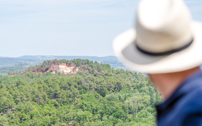 View of lush green hills near Moustier Sainte Marie, Provence, with a person in a hat in the foreground.