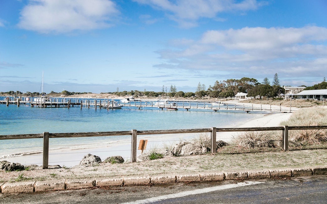 Boats docked at a pier on Rottnest Island, Australia, with sandy beach and clear blue water.