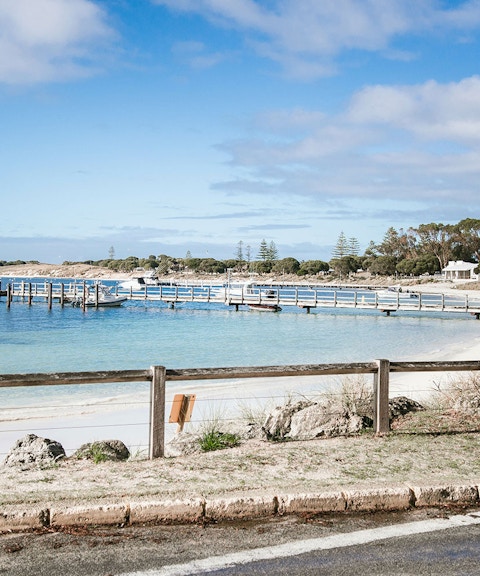 Boats docked at a pier on Rottnest Island, Australia, with sandy beach and clear blue water.