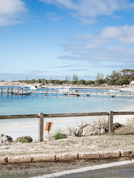 Boats docked at a pier on Rottnest Island, Australia, with sandy beach and clear blue water.