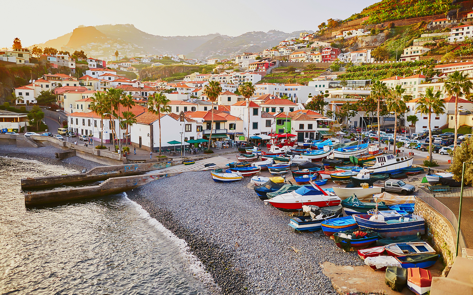 Colorful boats on a pebble beach in Madeira with hillside houses in the background.