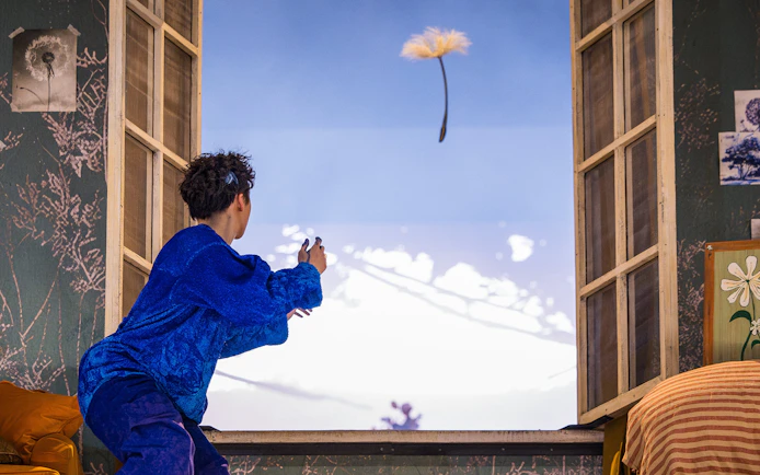 Performer in blue costume reaching towards floating dandelion during Cirque du Soleil Alizé show.