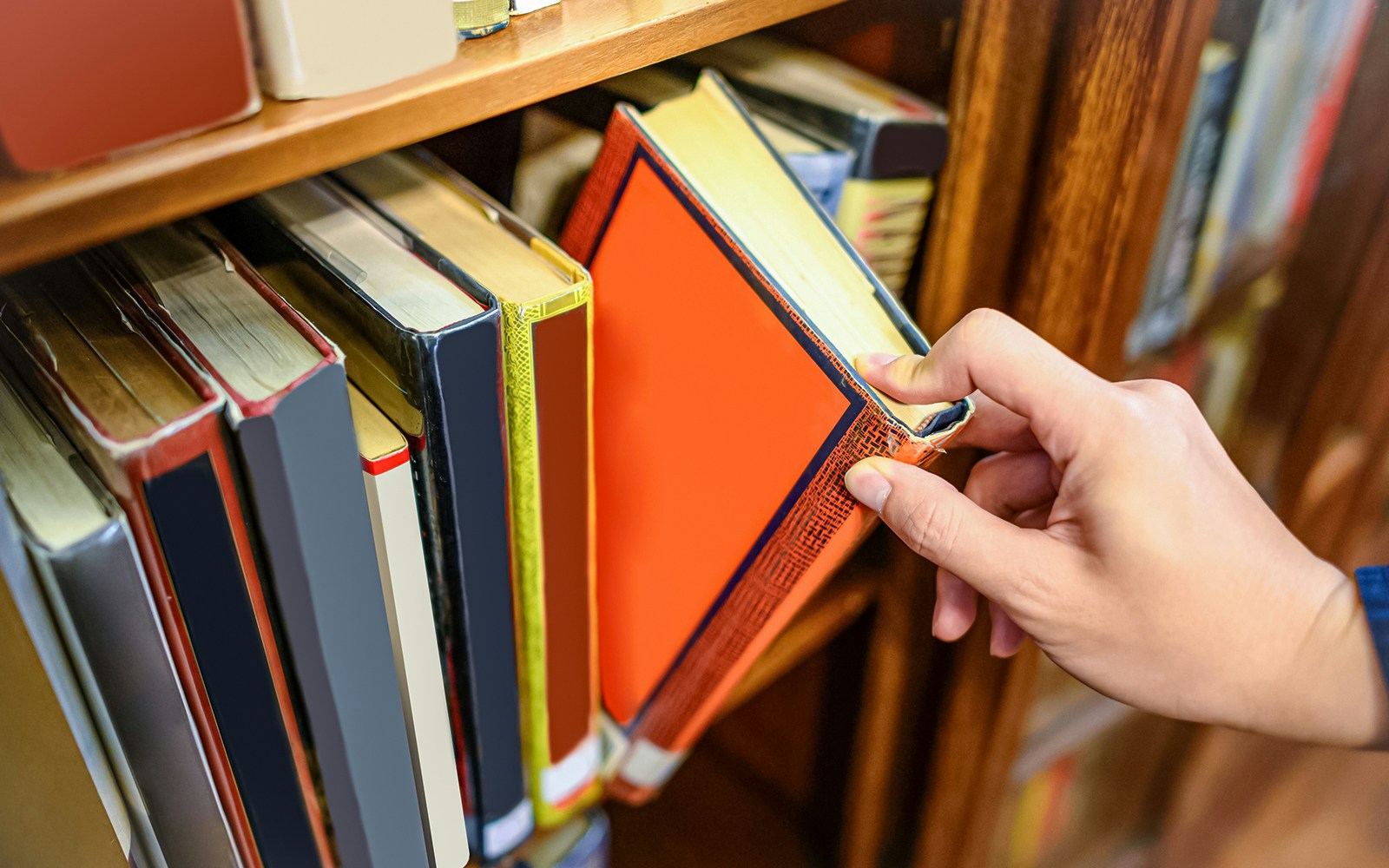 Hand selecting a book from a wooden bookshelf.