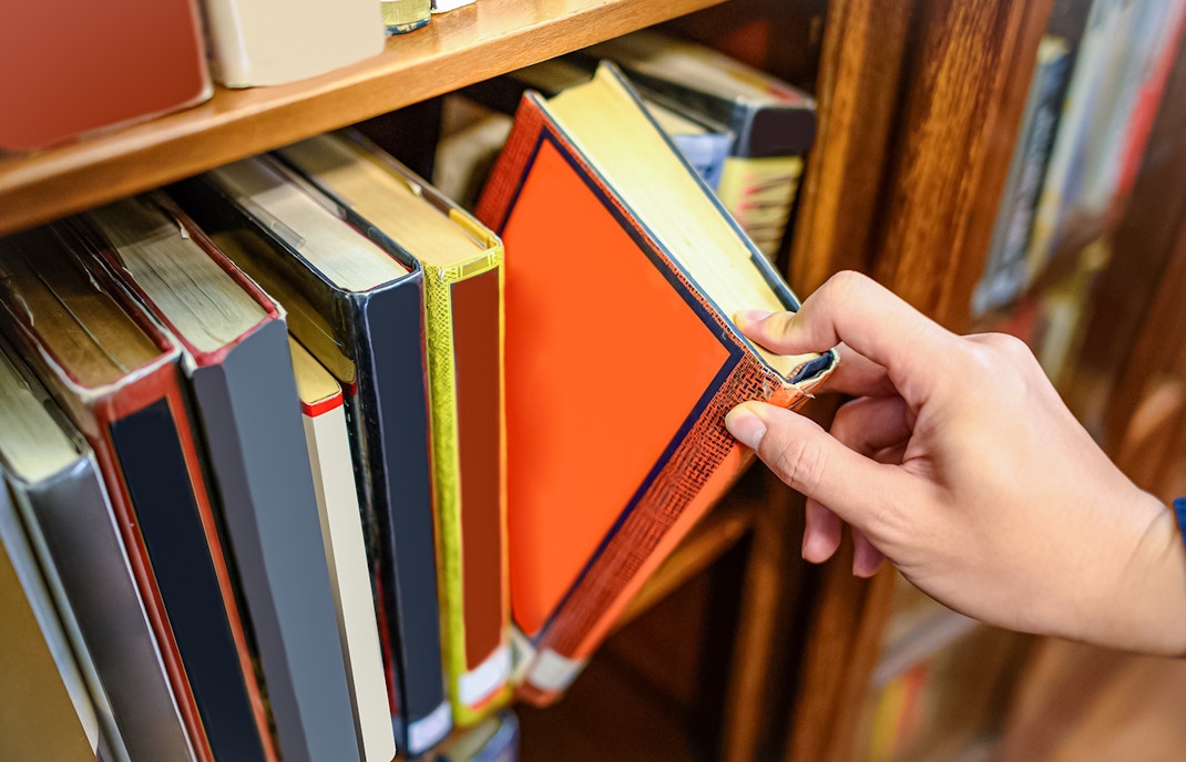 Hand selecting a book from a wooden bookshelf.
