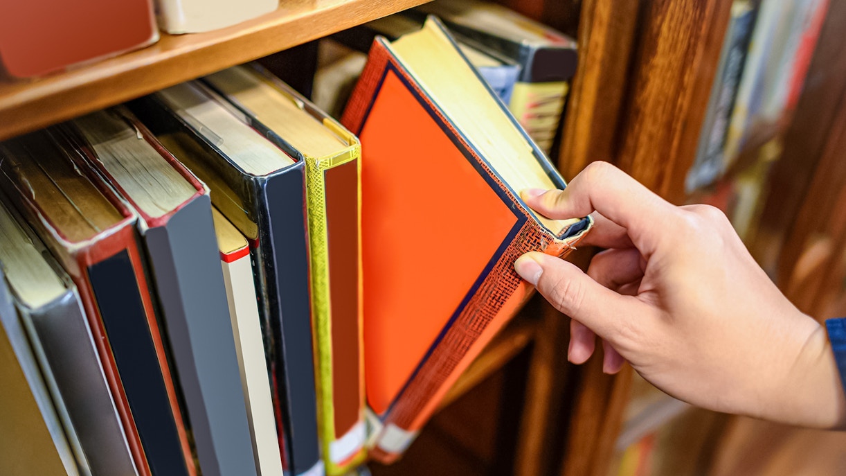 Hand selecting a book from a wooden bookshelf.