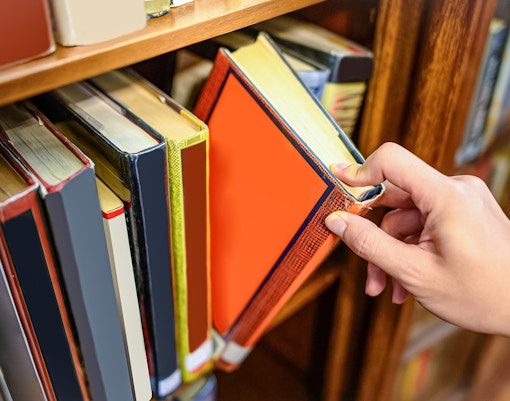 Hand selecting a book from a wooden bookshelf.
