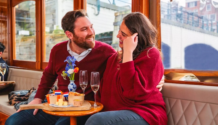 Couple enjoying a romantic cruise in Amsterdam with snacks and drinks.