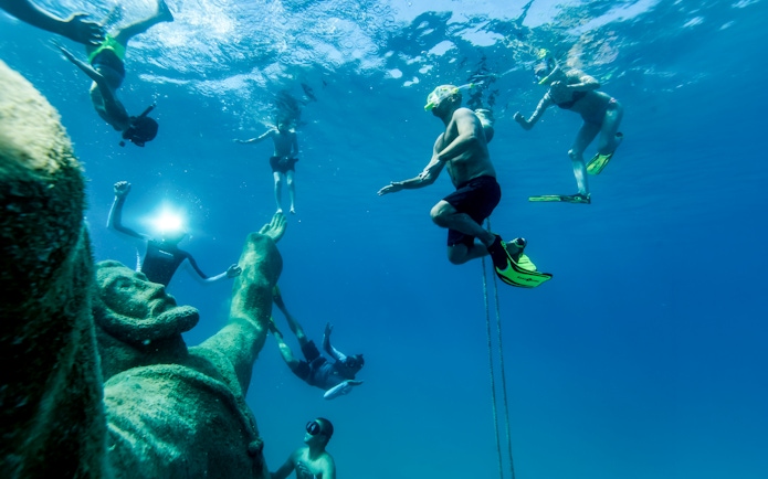 Snorkelers exploring underwater sculptures at a museum near a beach resort.
