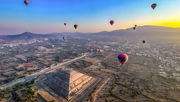 Hot air balloon floating above Teotihuacan Pyramid, Mexico, showcasing ancient ruins and scenic landscape.