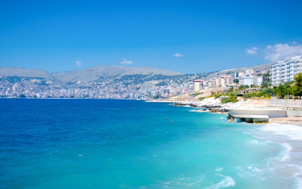 Ksamil beach with turquoise waters and distant view of coastal town, Albania.
