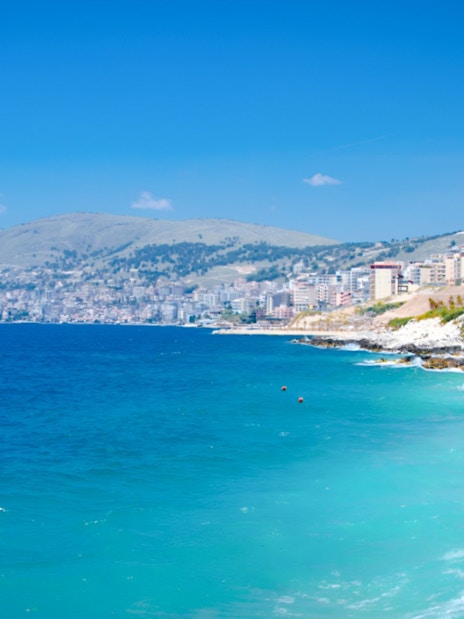 Ksamil beach with turquoise waters and distant view of coastal town, Albania.