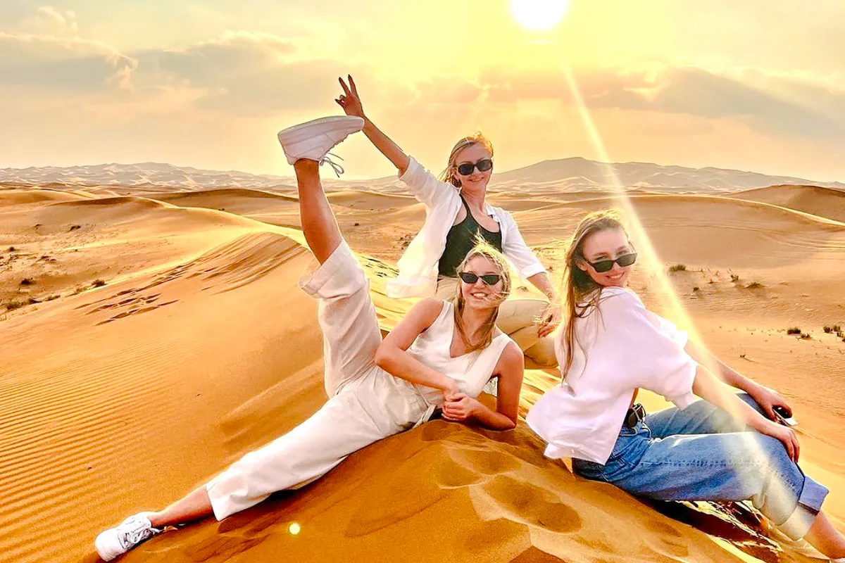 Group enjoying sunset on Abu Dhabi desert safari with camel ride and sandboarding.