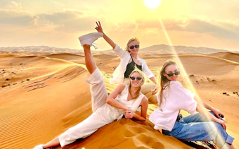 Group enjoying sunset on Abu Dhabi desert safari with camel ride and sandboarding.