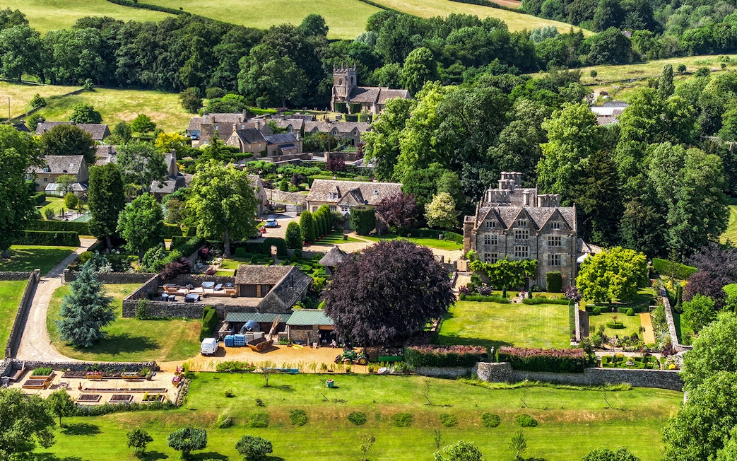 Aerial view of a Cotswolds village with historic stone buildings and lush gardens, Oxford tour.