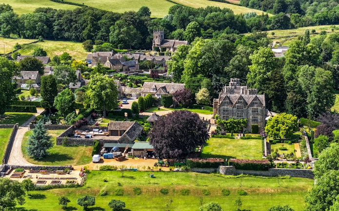 Aerial view of a Cotswolds village with historic stone buildings and lush gardens, Oxford tour.