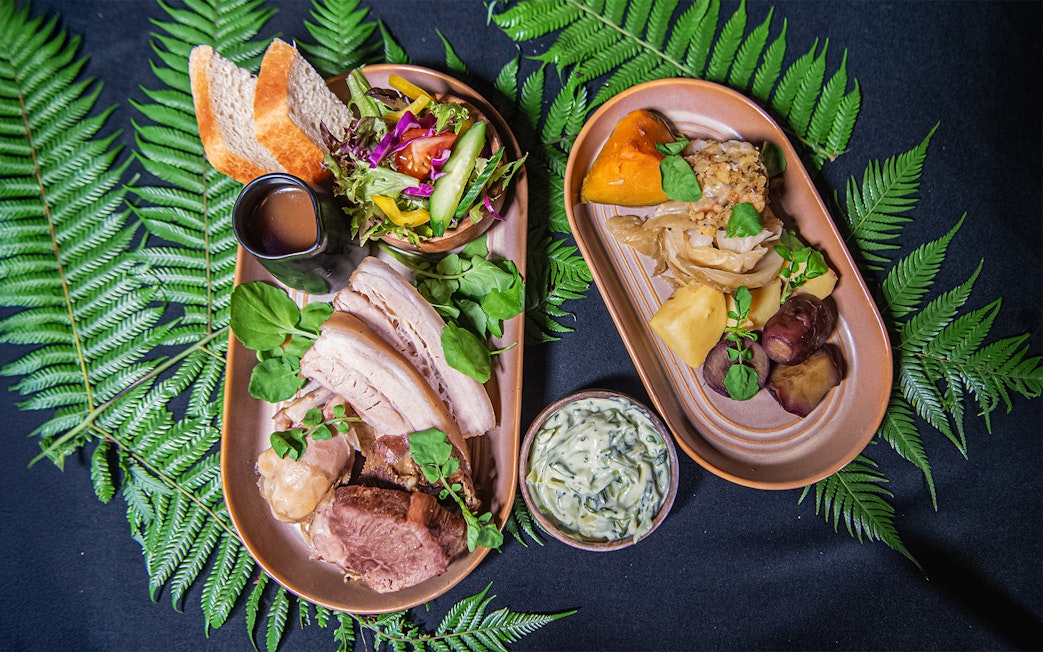 Two plated Hāngī meal with meats, vegetables, salad, and sauce on fern leaves.