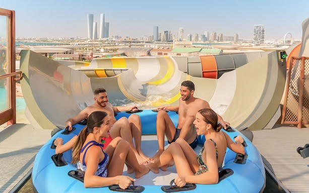 Visitors enjoying a group water ride at Meryal Waterpark with city skyline in background.