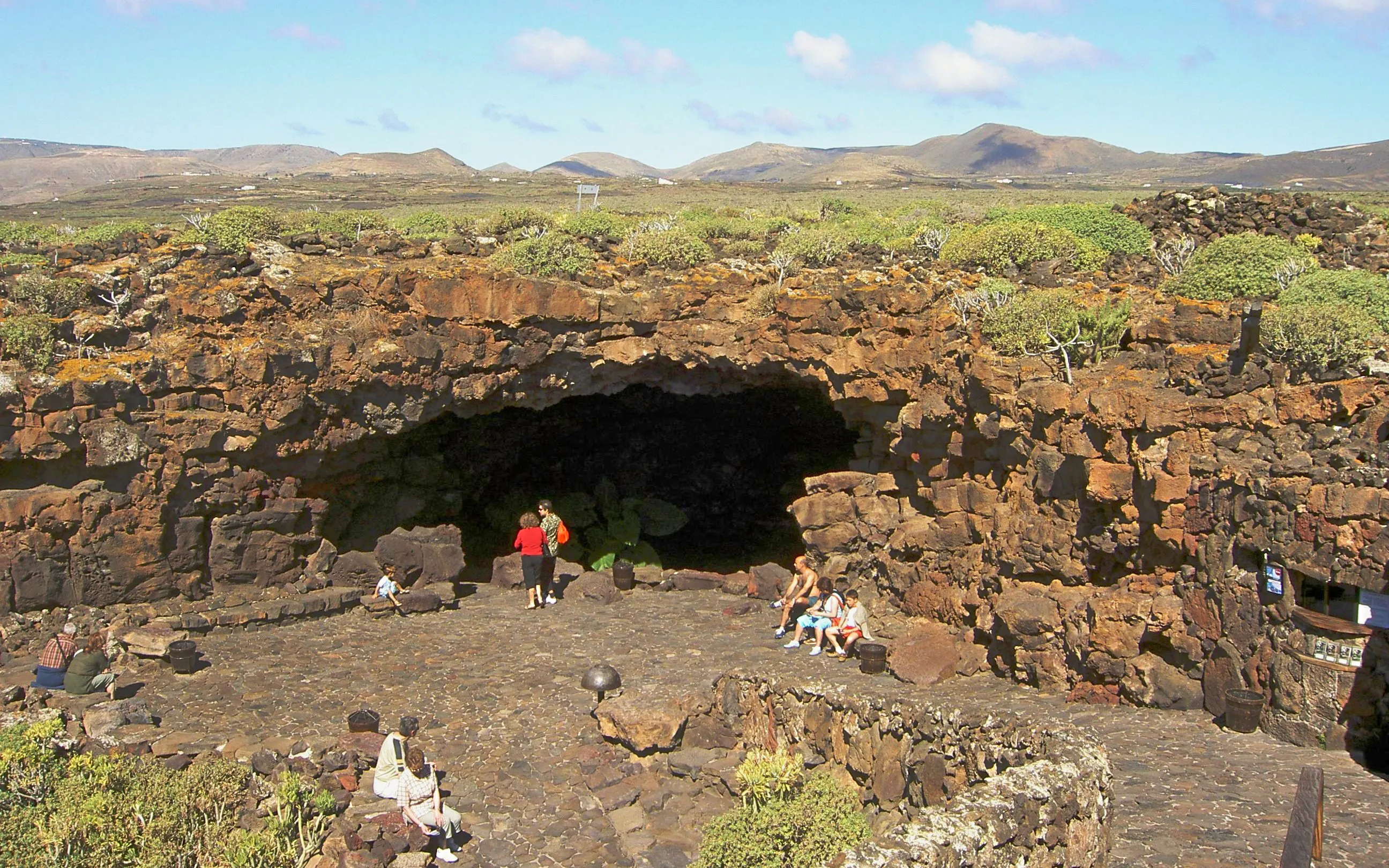 Cueva de los Verdes entrance with visitors on Lanzarote, surrounded by volcanic rock formations.