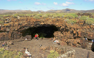 Cueva de los Verdes entrance with visitors on Lanzarote, surrounded by volcanic rock formations.