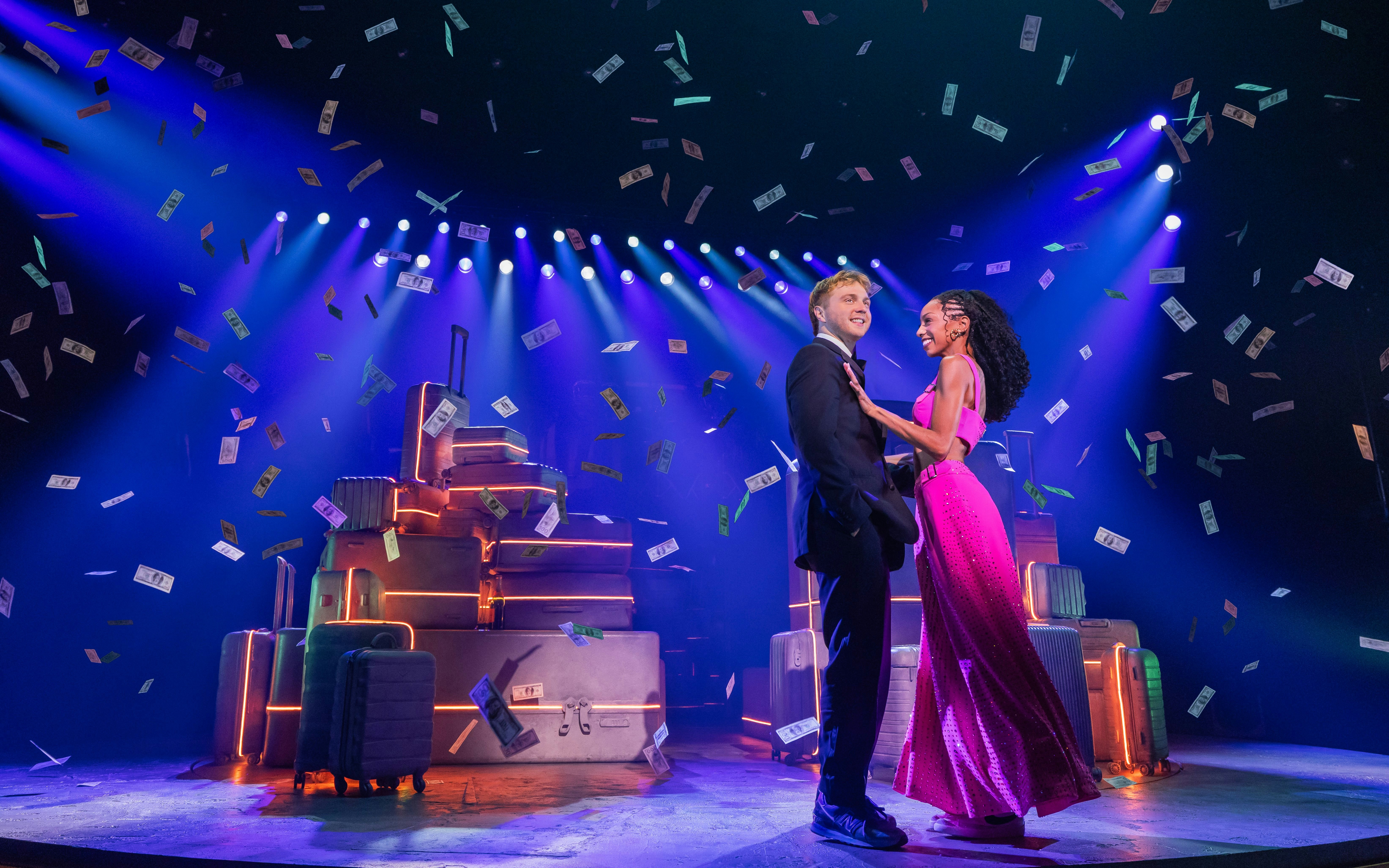 Actors performing in "Two Strangers (Carry a Cake Across New York)" on a Broadway stage with suitcases.