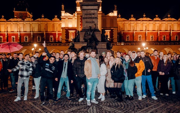 Group of people enjoying a night tour in Krakow's Main Square with historic architecture in the background.