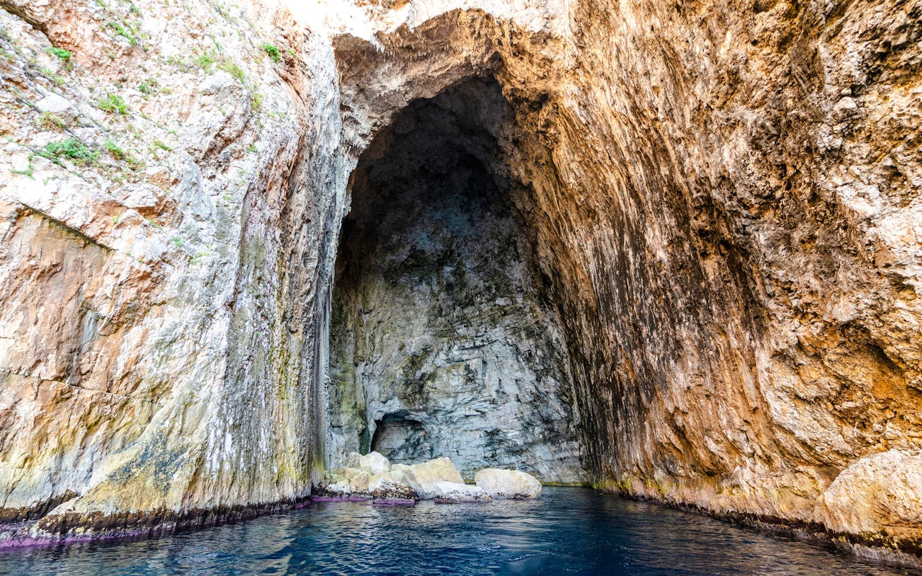 Haxhi Ali Cave entrance with rocky walls and blue water, Albania.