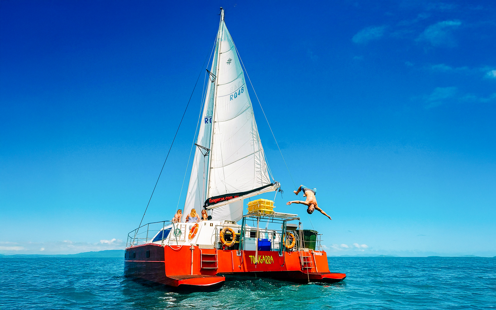 Sailing catamaran with tourists in Whitsundays, person diving into the sea.