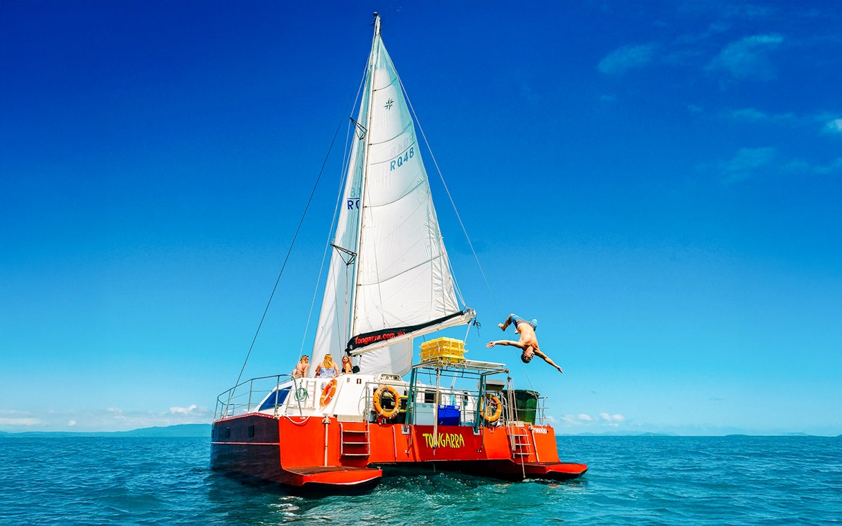 Sailing catamaran with tourists in Whitsundays, person diving into the sea.