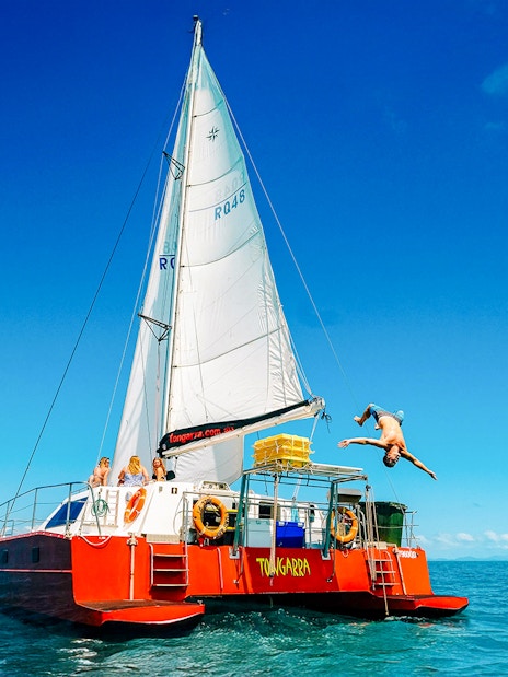 Sailing catamaran with tourists in Whitsundays, person diving into the sea.